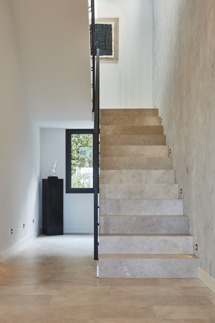 A stone staircase with metal handrail in high ceiling entrance. 