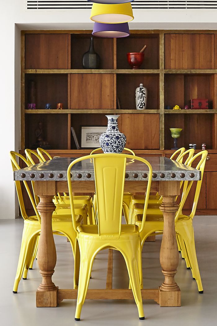 Yellow metal dining chairs around a zinc topped dining table with grey resin seamless flooring. 