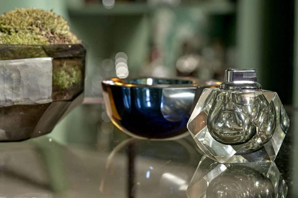 An upclose image on Murano glass table accessories next to an array of moss in a glass bowl, all adorned on a glass table.