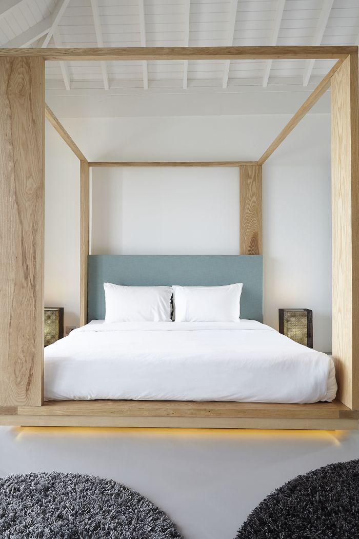 A natural oak custom four poster bed in room with painted white vaulted ceiling.