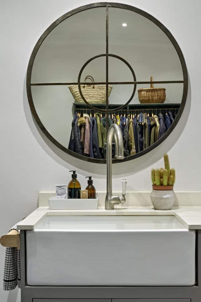 Round bronze mirror above a Belfast sink in a utility room.