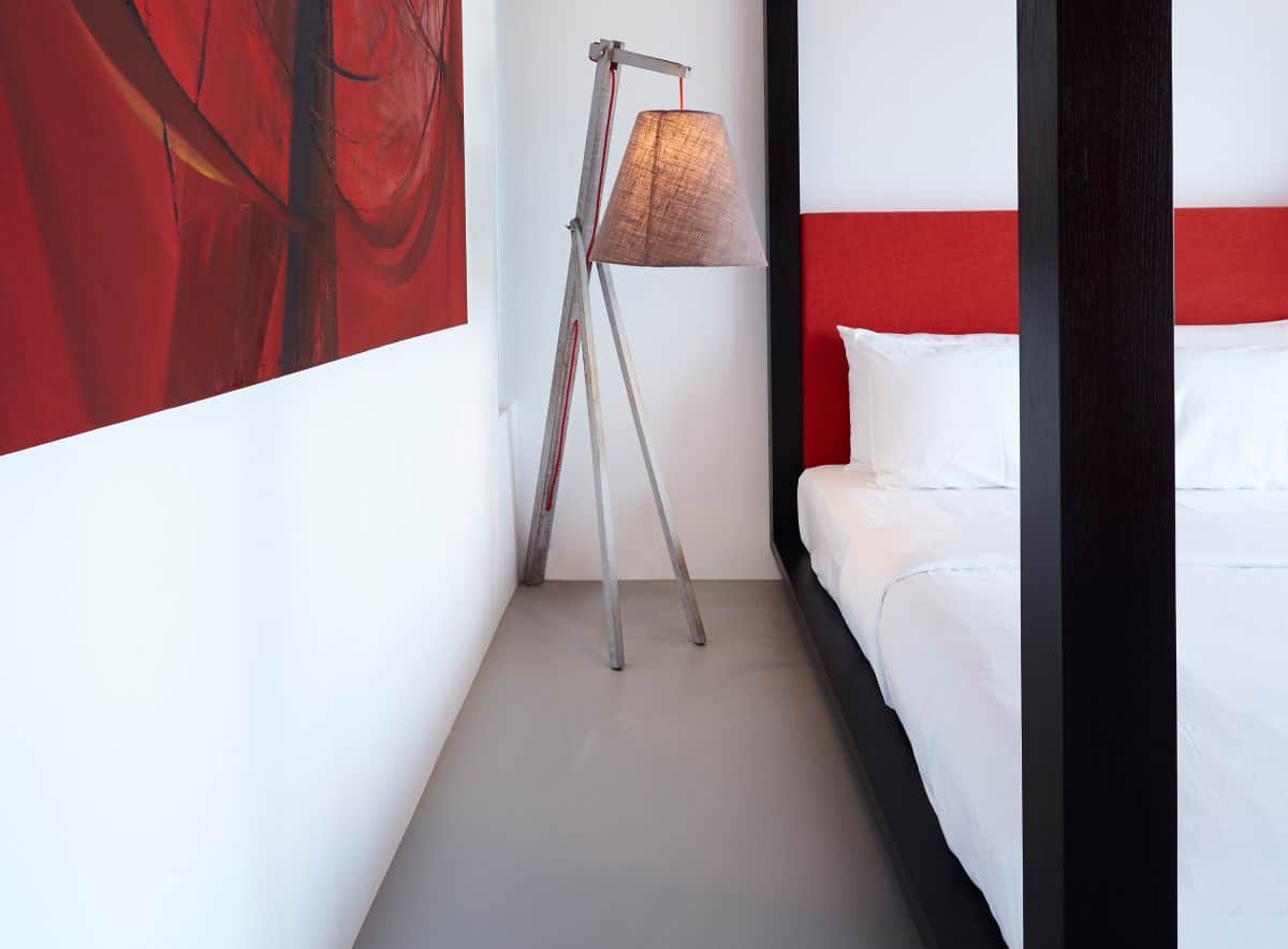 A black and red themed bedroom in a tropical villas with crisp white walls and grey resin flooring. 