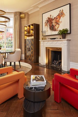 An image of two modern bright red and orange armchairs around a marble fireplace.