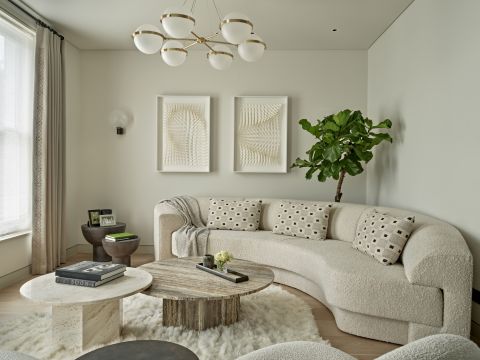 Curved sofa in drawing room with Gubi Pacha lounge chair and travertine coffee tables.