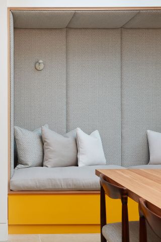 Reading nook in kitchen dining room with fabric padded panels and built in storage in yellow lacquer.