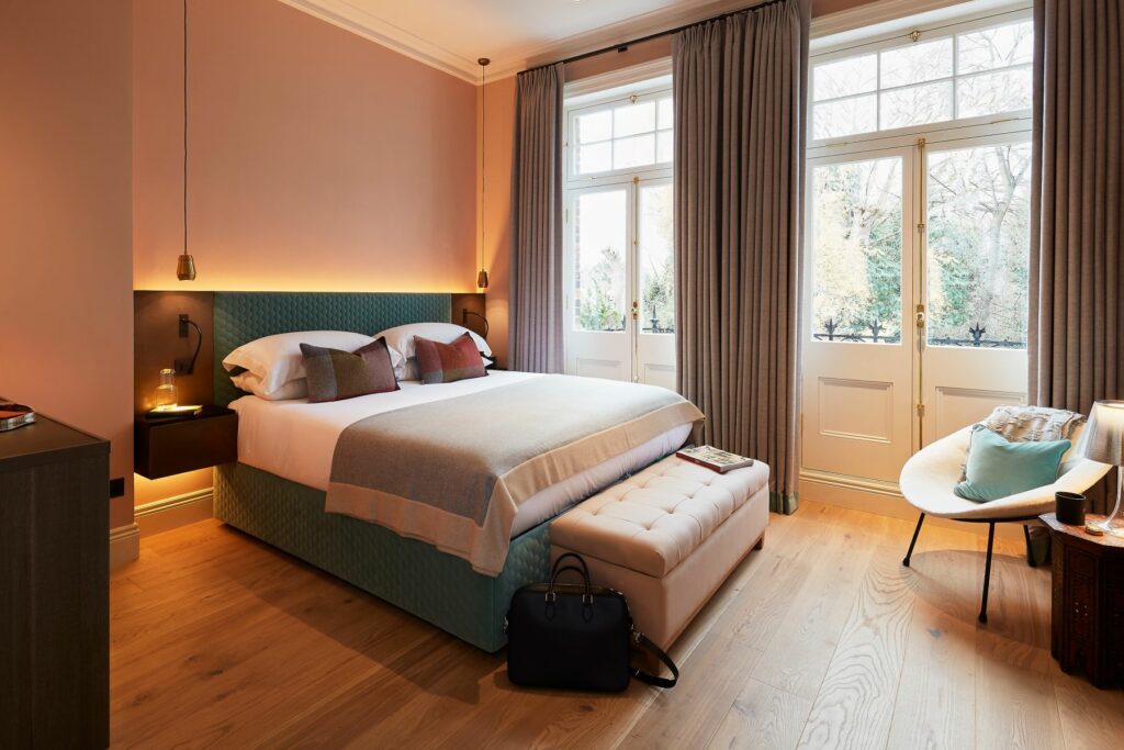 Large dusty pink master bedroom with french door windows and oak flooring.