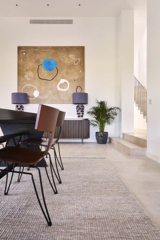 High ceiling neutral dining room with statement art piece above drinks console.