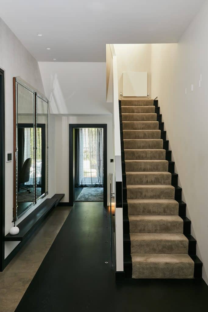 Chic hallway with two large mirrors leading to a staircase .