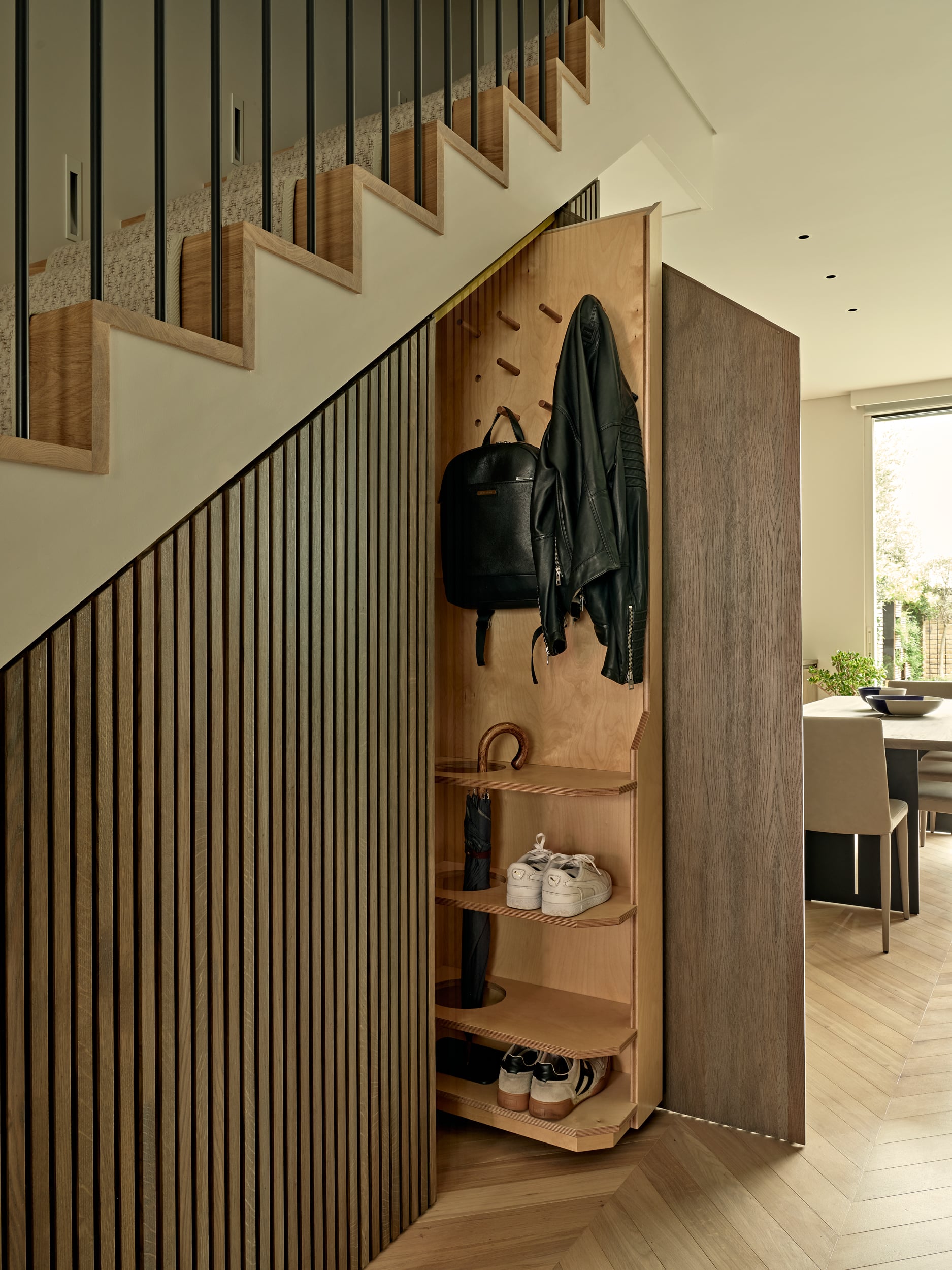 This luxurious under stairs showcases smart and efficient use of space. The slim paneled under stairs joinery features a pull-out storage unit, providing a practical solution for storing shoes, jackets, and bags. The light wood herringbone flooring harmonises with the light wood stairs, creating a cohesive and visually appealing look. A cream carpet running upstairs adds a touch of warmth and elegance. This cleverly designed under stairs room maximises functionality while maintaining a stylish and sophisticated atmosphere.