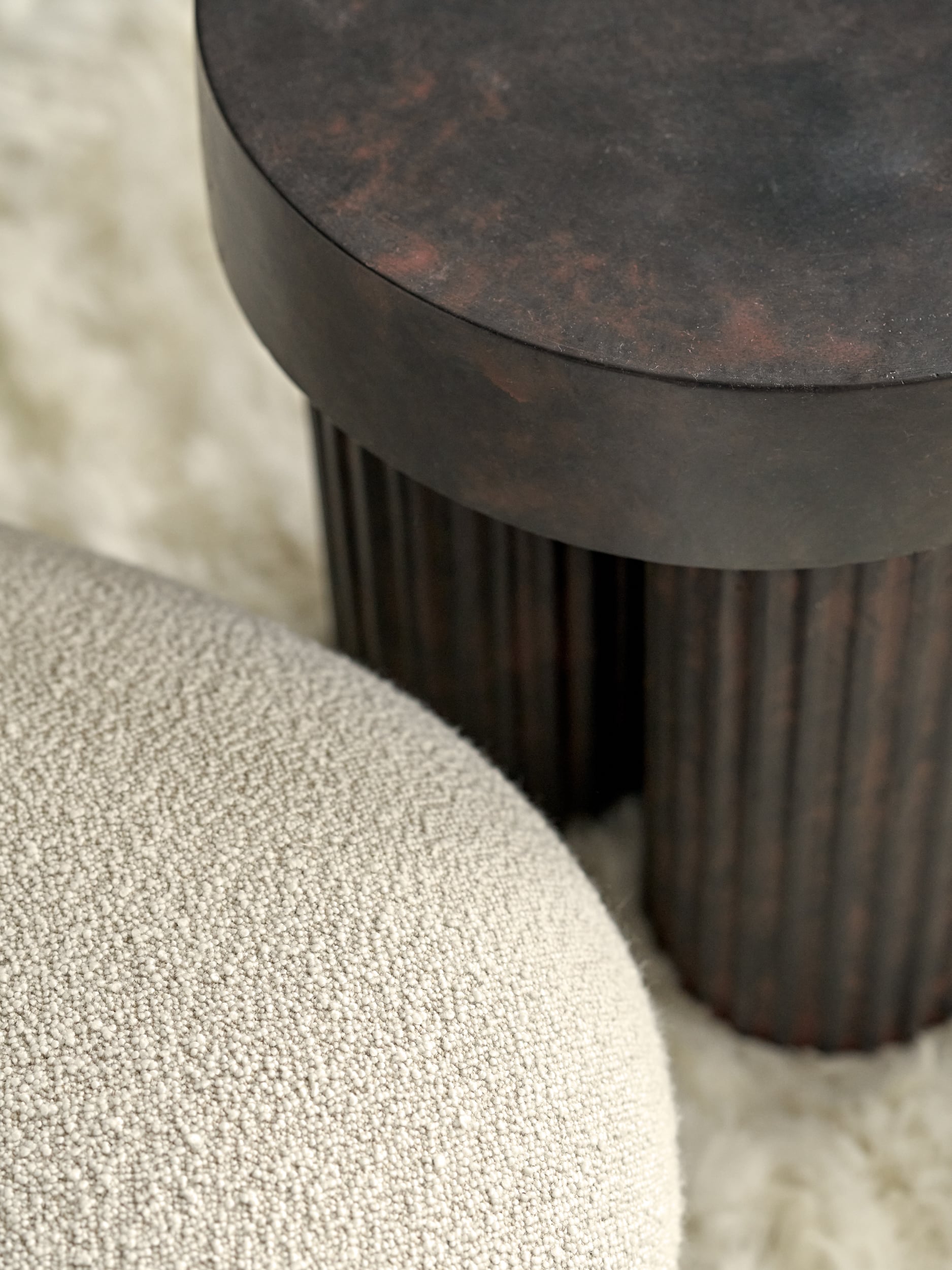 Luxurious drawing room showcasing an up close textures with a fluffy rug, boucle fabric armchair, and a dark stone three-legged side table.